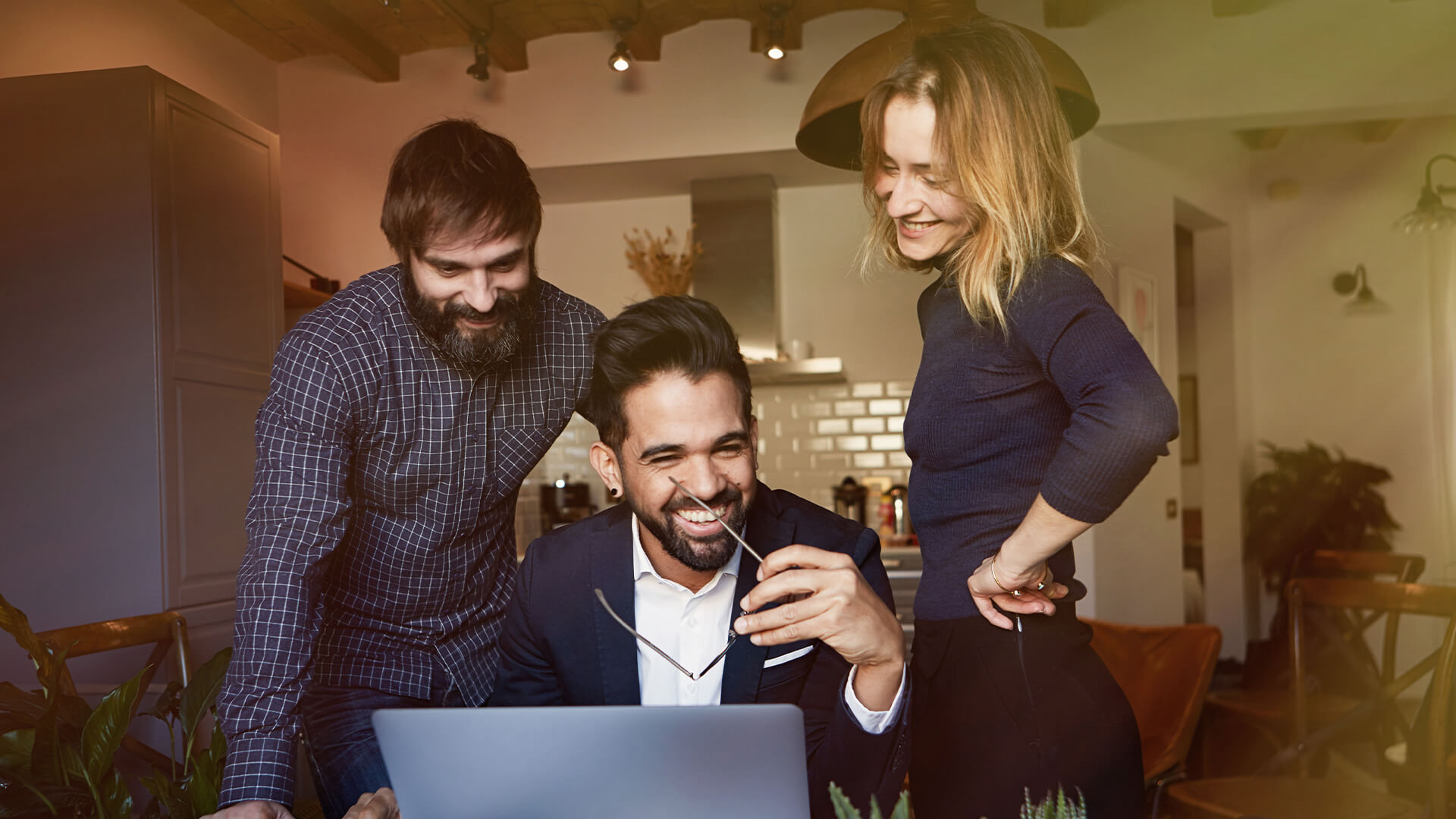 Three colleagues laughing together around a laptop